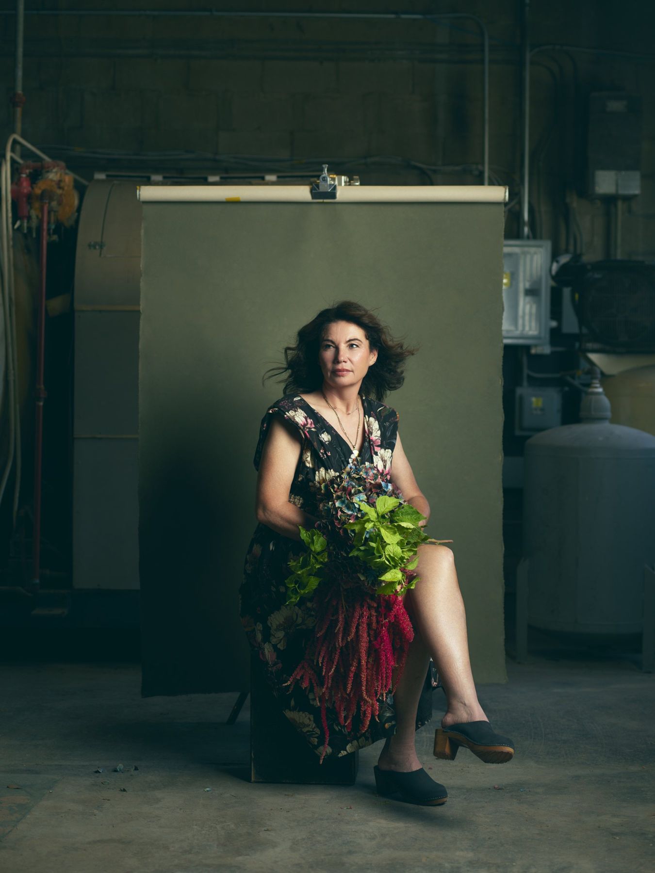 Andrea seated in the studio holding a bouquet of greenery and amaranth